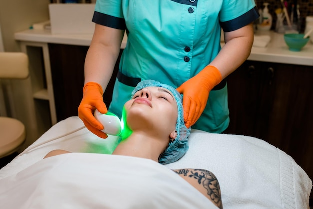 Cliente de mulher deitada na sala do salão de beleza recebe lifting facial não cirúrgico de ultra-som smas pelo médico esteticista profissional mão segurando o dispositivo de cosmetologia de hardware ultra-sônico para tratamento facial