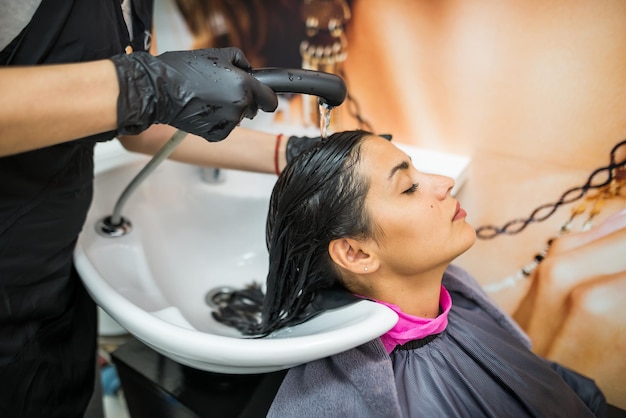 Cliente do sexo feminino lava o cabelo no salão cabeleireiro profissional lava a cabeça do cliente do sexo feminino com água e shampoo tratamento penteado beleza cuidados com o cabelo serviço de moda