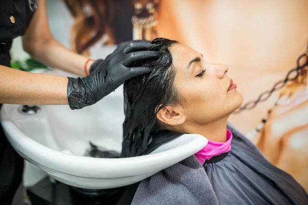 Cliente do sexo feminino lava o cabelo no salão cabeleireiro profissional lava a cabeça do cliente do sexo feminino com água e shampoo tratamento penteado beleza cuidados com o cabelo serviço de moda