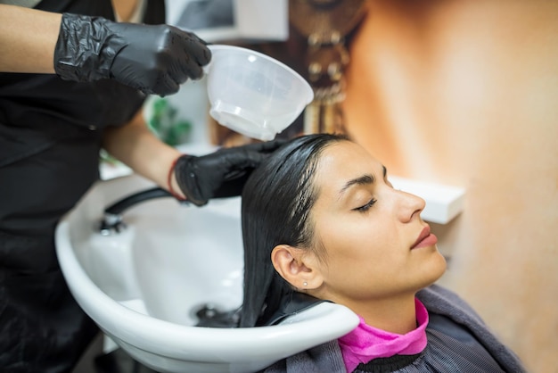 Cliente do sexo feminino lava o cabelo no salão cabeleireiro profissional lava a cabeça do cliente do sexo feminino com água e shampoo tratamento penteado beleza cuidados com o cabelo serviço de moda