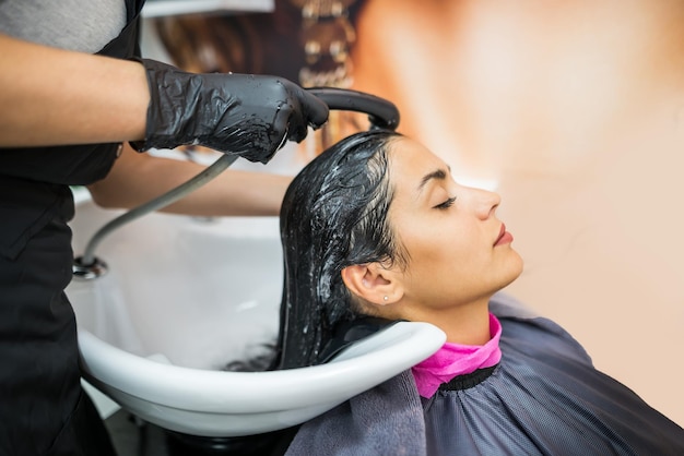 Cliente do sexo feminino lava o cabelo no salão cabeleireiro profissional lava a cabeça do cliente do sexo feminino com água e shampoo tratamento penteado beleza cuidados com o cabelo serviço de moda