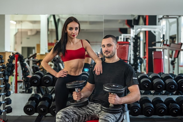 Cliente do sexo feminino malhando com um haltere sob o controle do personal trainer masculino na academia moderna