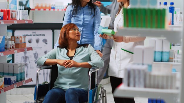 Foto cliente em cadeira de rodas recebendo ajuda de especialista, procurando comprar medicamentos prescritos e suplementos. mulher com deficiência que vem à farmácia com assistente social, precisando de comprimidos ou drogas.