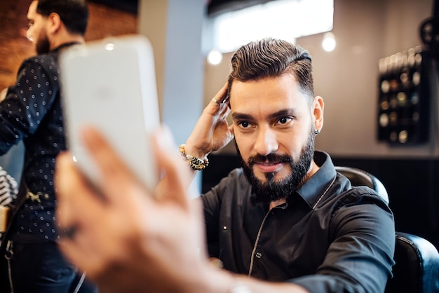 Foto cliente examinando el corte de pelo en el teléfono móvil en el salón