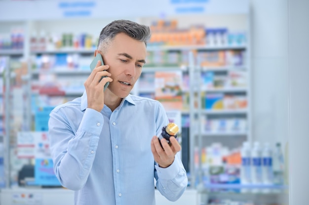 Cliente de farmacia con un suplemento dietético hablando por teléfono inteligente