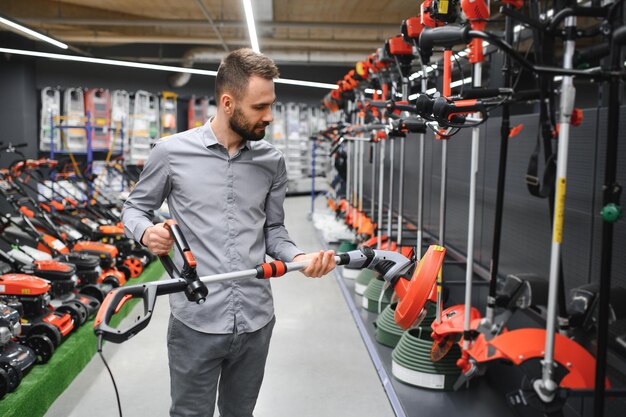 Foto cliente feliz con cortador de césped eléctrico en las manos en la tienda de equipos de jardín