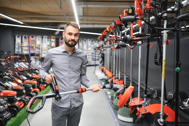 Foto cliente feliz con cortador de césped eléctrico en las manos en la tienda de equipos de jardín