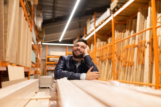 Cliente feliz en una ferretería mira estantes con tablones y bloques de madera con madera contrachapada y