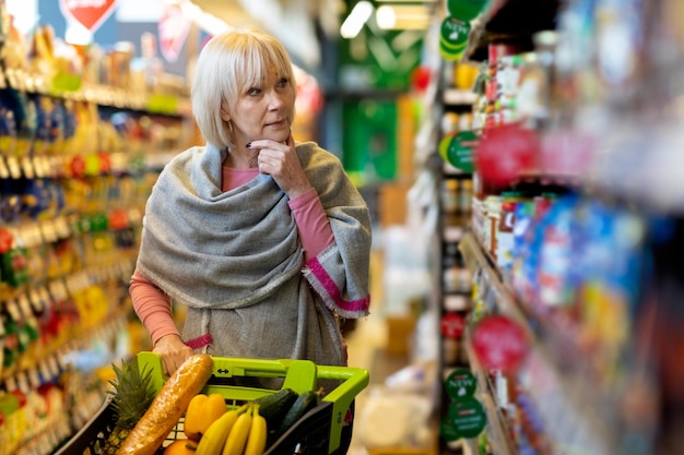 Cliente femenino confundido mirando el estante con salsas en el supermercado