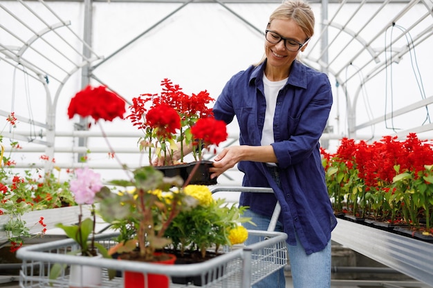 Cliente feminino de estufa coloca flores em vasos no carrinho de compras