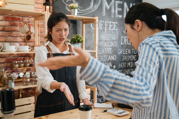 cliente feminino emocional discutindo com a funcionária no balcão do bar. Visitante insatisfeito irritado com o serviço no café. cliente mulher não gosta de beber café e gritar com a senhora barista na loja da manhã