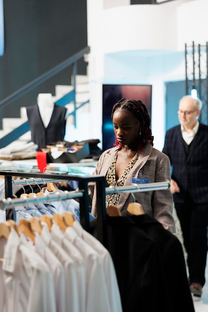 Cliente grávida olhando roupas da moda em cabides, comprando roupas de gravidez na boutique moderna. Mulher afro-americana comprando mercadorias da moda em loja de roupas. conceito de moda