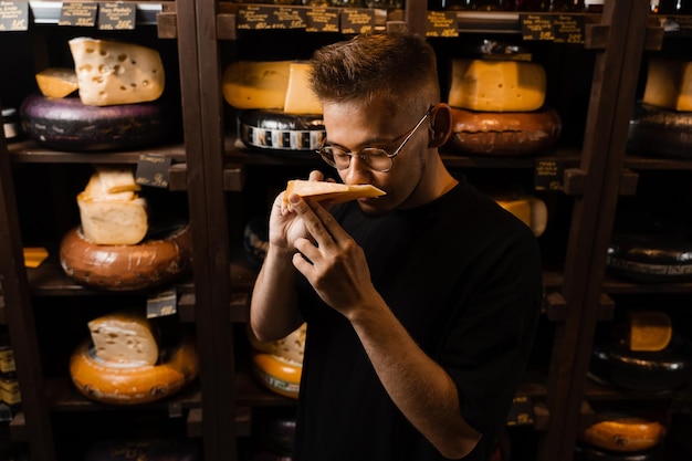 Cliente guapo en la tienda de queso huele y disfruta de queso gouda limitado Aperitivo sabroso trozo de queso para aperitivo