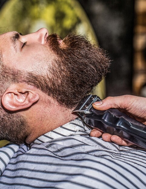 Cliente inconformista obteniendo corte de pelo Manos de un peluquero con un primer plano de la cortadora de barba Hombre barbudo