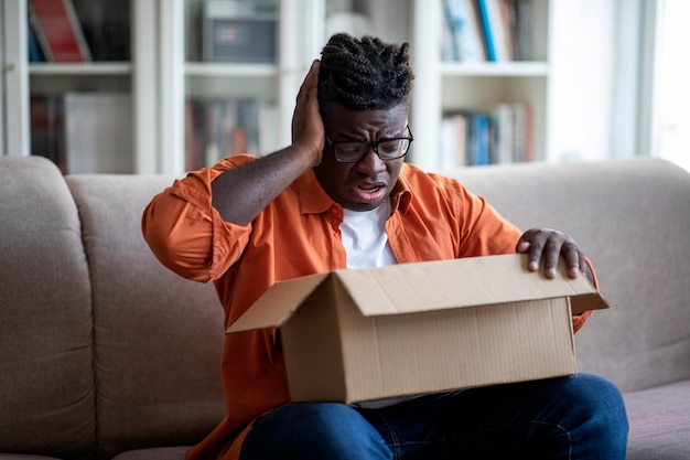 Cliente jovem afro-americano desapontado abrindo caixa de encomendas