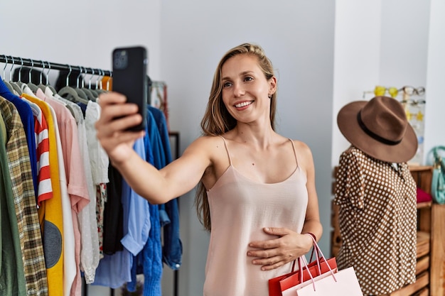 Cliente jovem caucasiana faz selfie pelo smartphone fazendo compras na loja de roupas