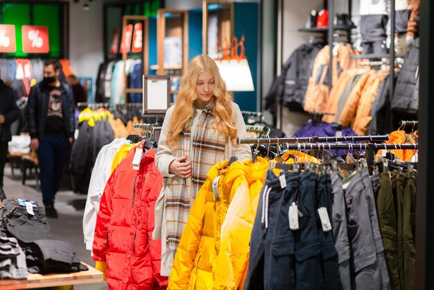 Cliente jovem com cabelo dourado escolhendo roupas em loja de roupas modernas