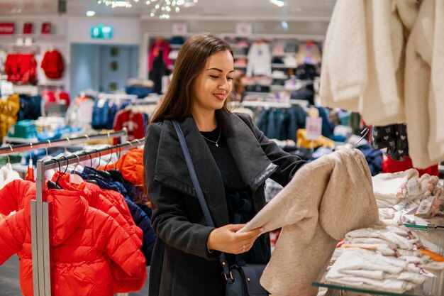 Cliente joven eligiendo ropa de bebé o ropa infantil en la tienda. Comprar en la tienda para niños pequeños