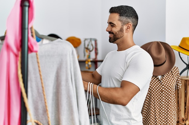 Foto cliente joven hispano eligiendo ropa de compras en la tienda de ropa