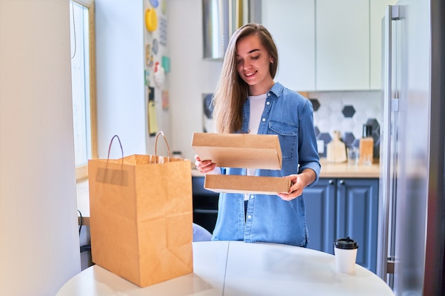 Cliente joven milenario sonriente feliz adulto lindo casual moderno recibió bolsas de cartón con comida para llevar y bebidas en casa. Concepto de servicio de entrega rápida