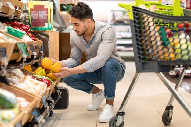 Cliente masculino árabe haciendo compras de comestibles eligiendo verduras en el supermercado