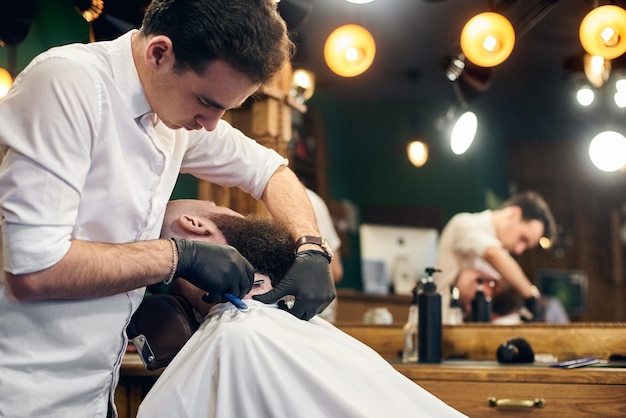 Cliente masculino con barba sentado en silla de peluquería Hombre serio con larga barba marrón Estilo moderno y popular de leñador