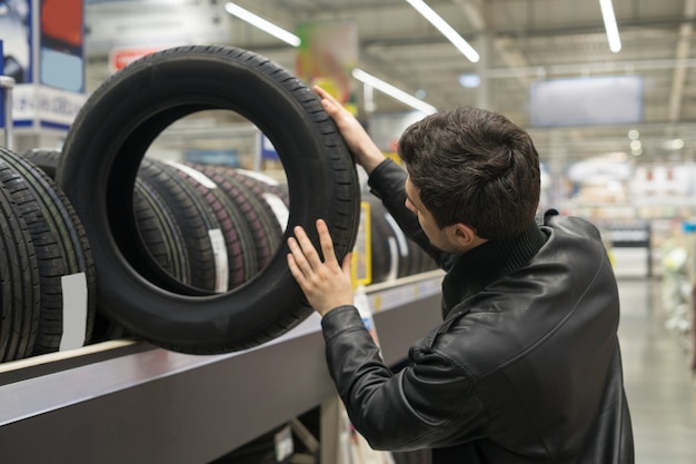 Cliente masculino eligiendo neumáticos nuevos en el supermercado