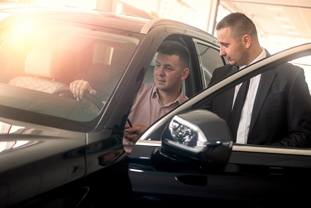 Cliente masculino y gerente hablando cerca del vehículo sobre la compra en el concepto de venta de concesionarios de automóviles