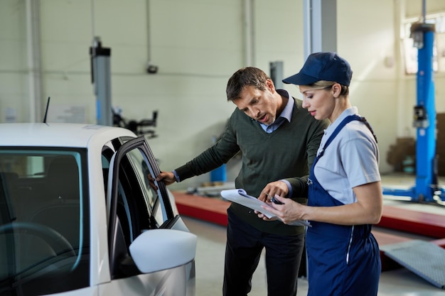 Cliente masculino y mecánico femenino analizando datos de automóviles en taller de reparación de automóviles