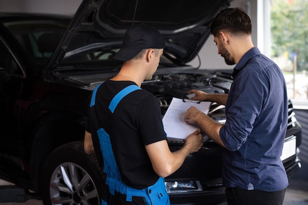 Foto el cliente y el mecánico discuten el próximo acuerdo de reparación de servicio automático de reparación de automóviles y el concepto de personas