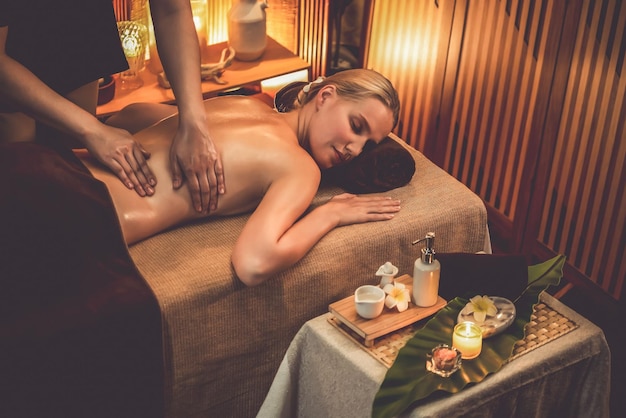 Cliente mujer caucásica disfrutando de un relajante masaje de spa antiestrés y mimándose con la recreación de la piel de belleza en un cálido salón de belleza con iluminación de velas en un spa de lujo en un resort u hotel tranquilo