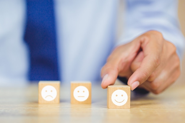 Cliente presionando emoticon de cara sonriente en cubo de madera