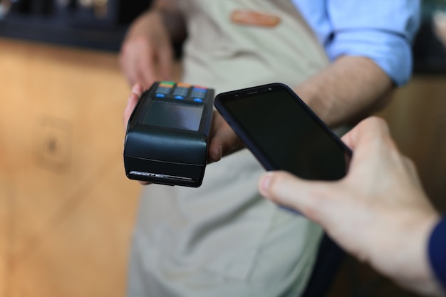 Foto cliente que usa el teléfono inteligente para el pago al propietario en el restaurante cafetería, tecnología sin efectivo.