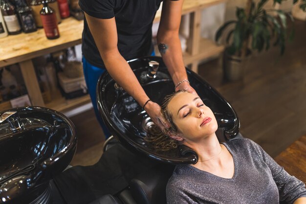 Cliente relajado con su cabello lavado con champú por un peluquero en el lavabo de la barbería