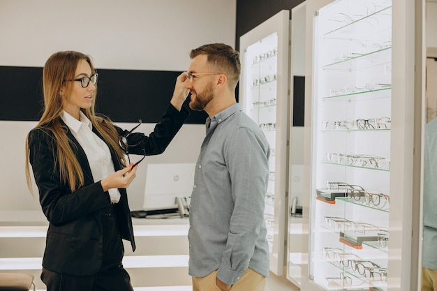 Cliente shoosing anteojos en tienda óptica con la ayuda del vendedor