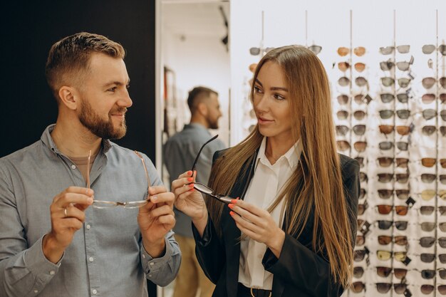 Cliente shoosing anteojos en tienda óptica con la ayuda del vendedor