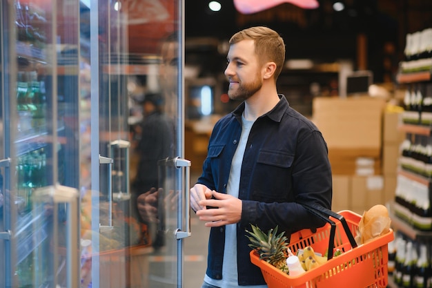 Cliente En El Supermercado Hombre Haciendo Compras De Comestibles De Pie Con El Carro Eligiendo Productos Alimenticios En El Interior Chico Comprando Comestibles En La Tienda De Alimentos Enfoque Selectivo Espacio De Copia