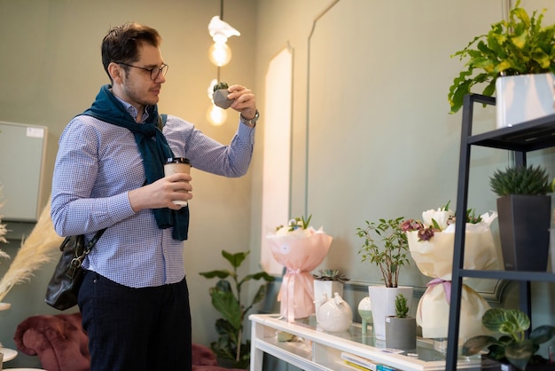 Un cliente de una tienda de flores frescas y macetas examina un pequeño cactus en una maceta