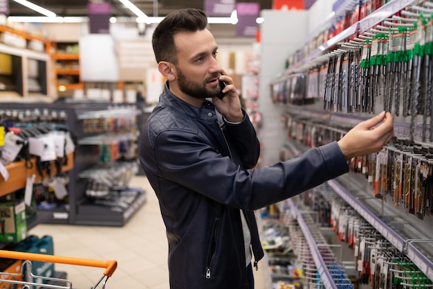 Un cliente en una tienda de herramientas elige un taladro para metal hablando por teléfono