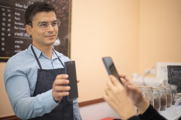 Cliente usando telefone para pagamento ao proprietário no conceito de pagamento de tecnologia sem dinheiro do restaurante café