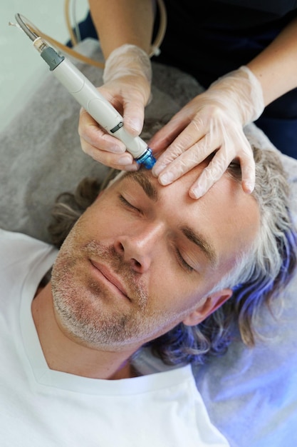 Cliente varón de mediana edad durante una limpieza facial profunda en una clínica de cosmetología