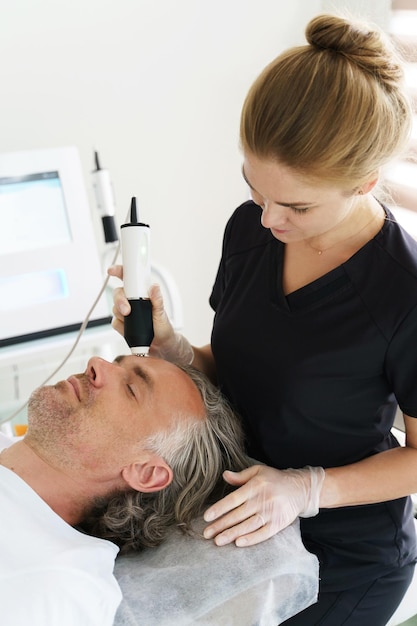 Cliente varón de mediana edad durante el rejuvenecimiento con láser de dióxido de carbono en una clínica de cosmetología