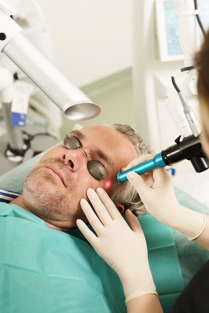 Foto cliente varón de mediana edad durante el tratamiento con láser en una clínica médica estética