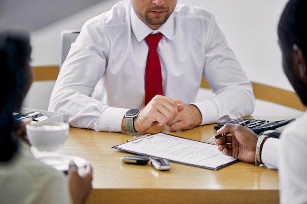 Los clientes negros firman un contrato mientras están sentados a la mesa con el vendedor