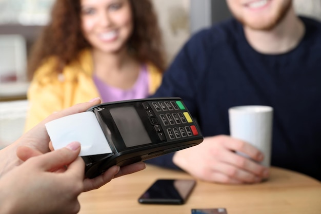 Foto clientes que usan una máquina de tarjetas de crédito para pagos que no son en efectivo en el primer plano de la cafetería