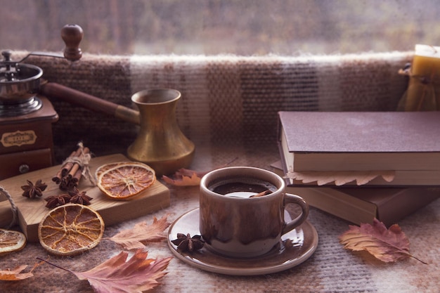 Clima de outono atmosfera de outono Uma xícara de café quente paus de canela anis estrelado um livro folhas de outono em uma manta de malha em um dia chuvoso