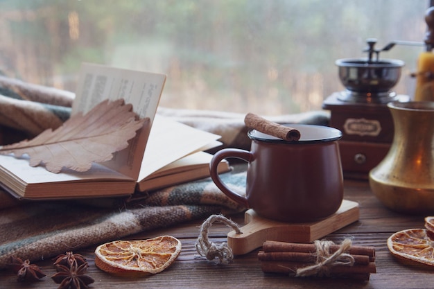 Clima de outono atmosfera de outono Uma xícara de café quente um cobertor xadrez um moinho de café paus de canela anis estrelado um livro em um parapeito de madeira em um dia chuvoso