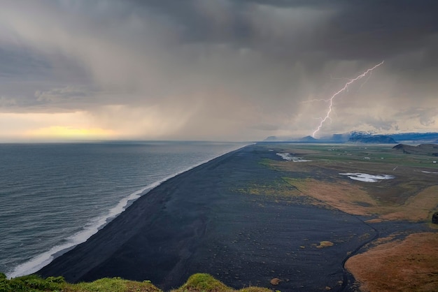 Clima relámpago sobre la playa de arena negra contra el cielo nublado durante la puesta de sol