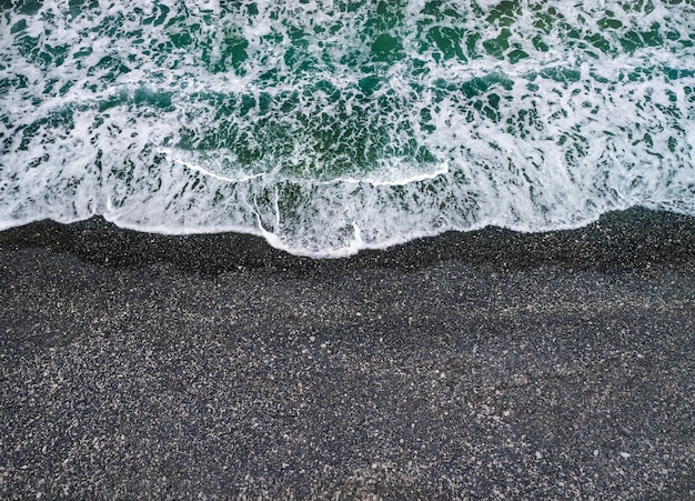 Clima tempestuoso, ondas do mar quebrando em uma costa com areia preta vulcânica, fundo com espaço de cópia