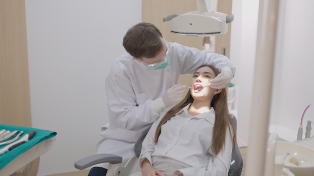 En una clínica dental una vista lateral de un dentista en uniforme que trata los dientes de una paciente